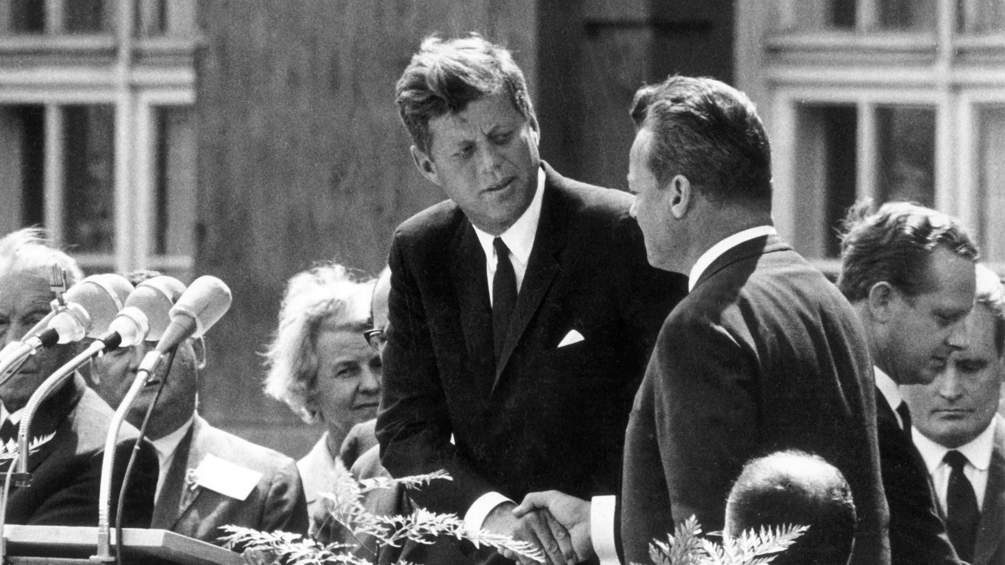 US-Präsident John F. Kennedy (M.) reicht dem Regierenden Bürgermeister von Berlin, Willy Brandt (rechts neben ihm), vor dem Schöneberger Rathaus in Berlin am 26. Juni 1963 die Hand. Mit dem legendären deutsch gesprochenen Satz "Ich bin ein Berliner" drückte Kennedy in seiner Rede seine Verbundenheit mit den Menschen in der geteilten Stadt aus.