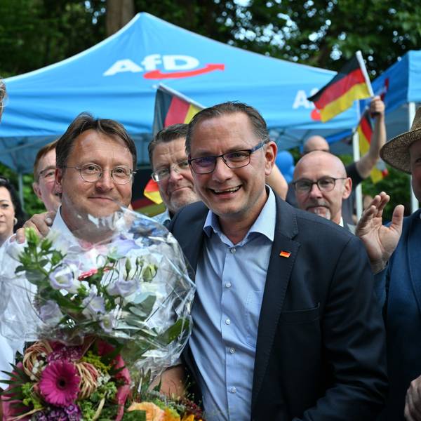 Björn Höcke (links), Vorsitzender der AfD Thüringen, und Tino Chrupalla, AfD-Bundesvorsitzender (rechts), gratulieren dem Wahlsieger Robert Sesselmann. Er hält einen Blumenstrauß in der Hand.
