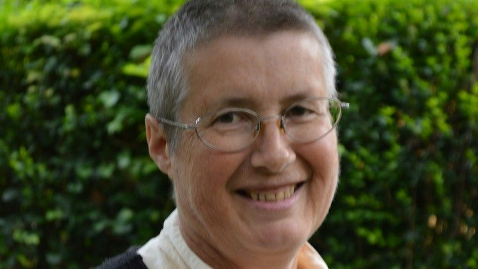 Alix Otten, eine britische Rentnerin mit Kurzhaarfrisur und Brille, lächelt in die Kamera