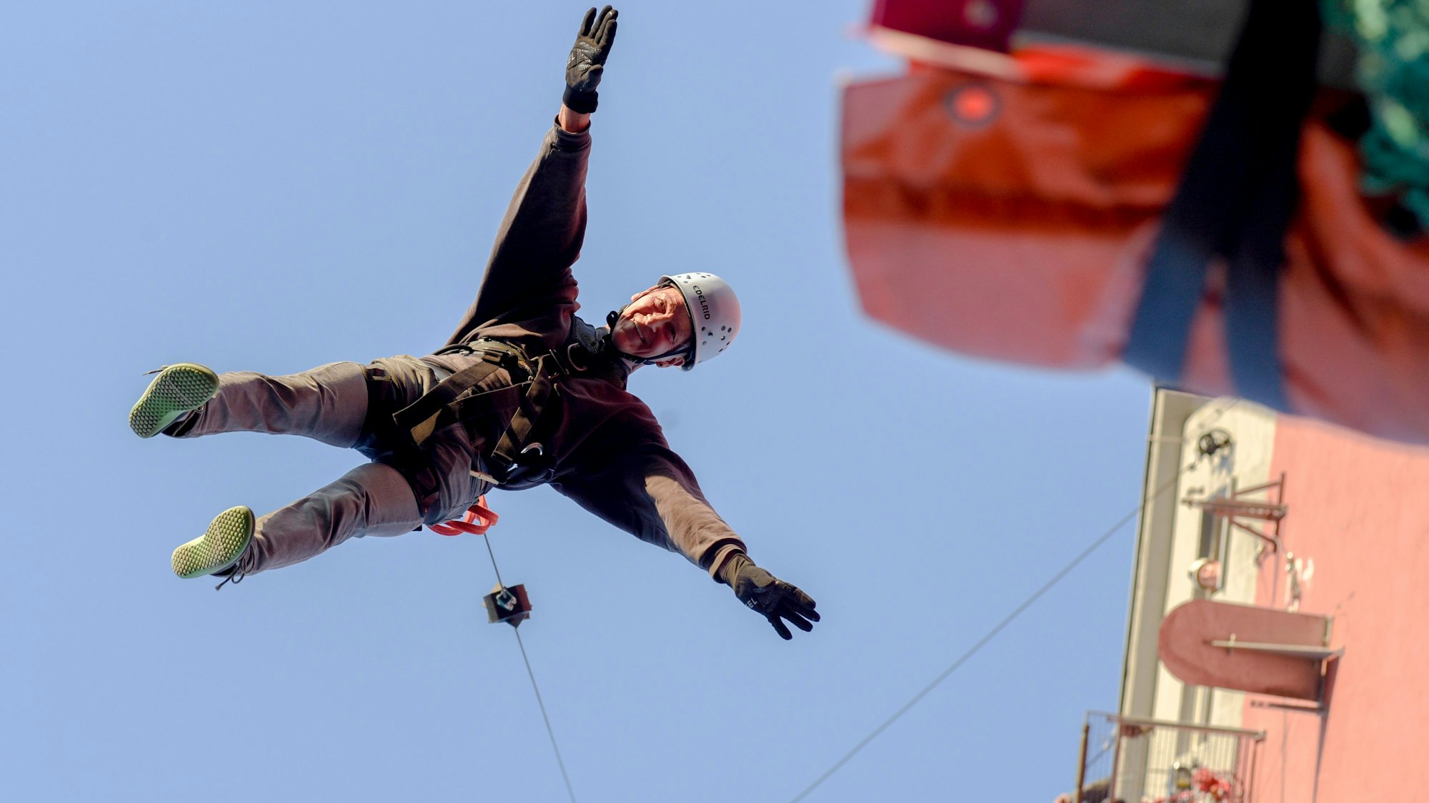 Das Foto zeigt einen Mann im Geschirr im freien Fall vor dem Kletterturm.