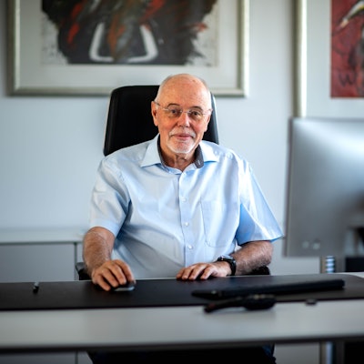 Ein Mann mit einem Kurzarmhemd sitzt an einem aufgeräumten Schreibtisch.