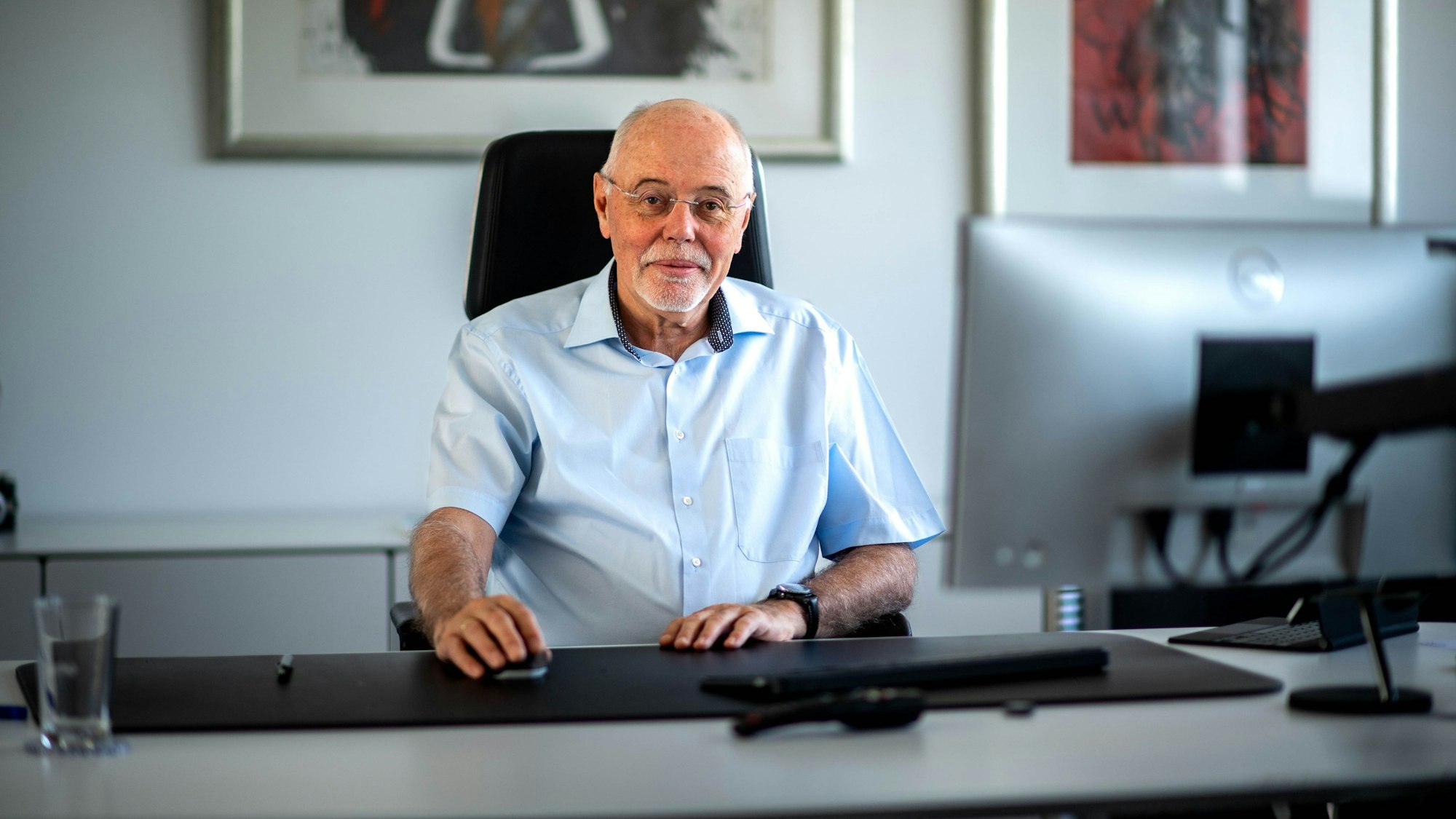 Ein Mann mit einem Kurzarmhemd sitzt an einem aufgeräumten Schreibtisch.