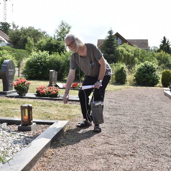 Ein älterer Mann deutet auf ein Grab auf einem Friedhof.