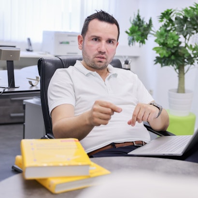 Toni Lushaj, Inhaber der MPU-Vorbereitungsstelle MPU Köln, im Beratungsgespräch mit einem Klienten. Er gestikuliert. Der Klient ist verschwommen von hinten zu sehen.