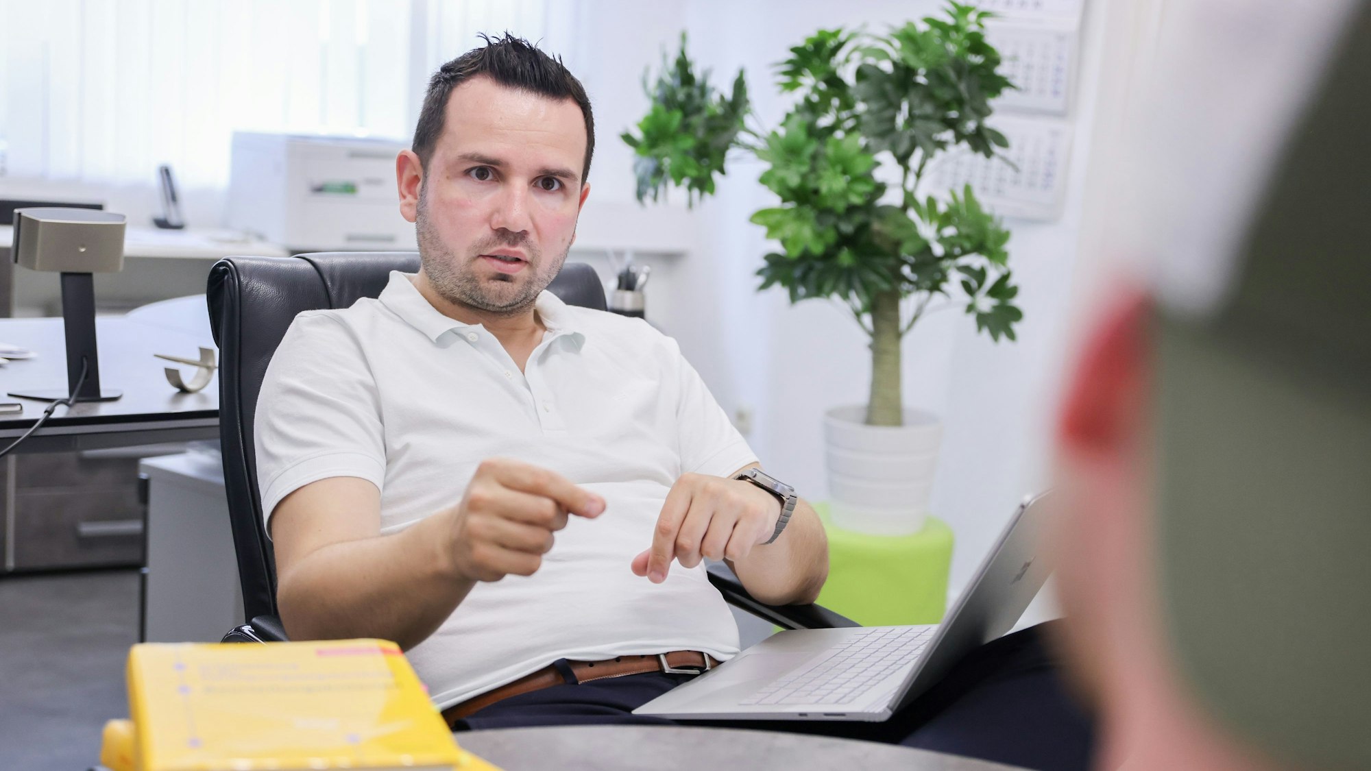 Toni Lushaj, Inhaber der MPU-Vorbereitungsstelle MPU Köln, im Beratungsgespräch mit einem Klienten. Er gestikuliert. Der Klient ist verschwommen von hinten zu sehen.