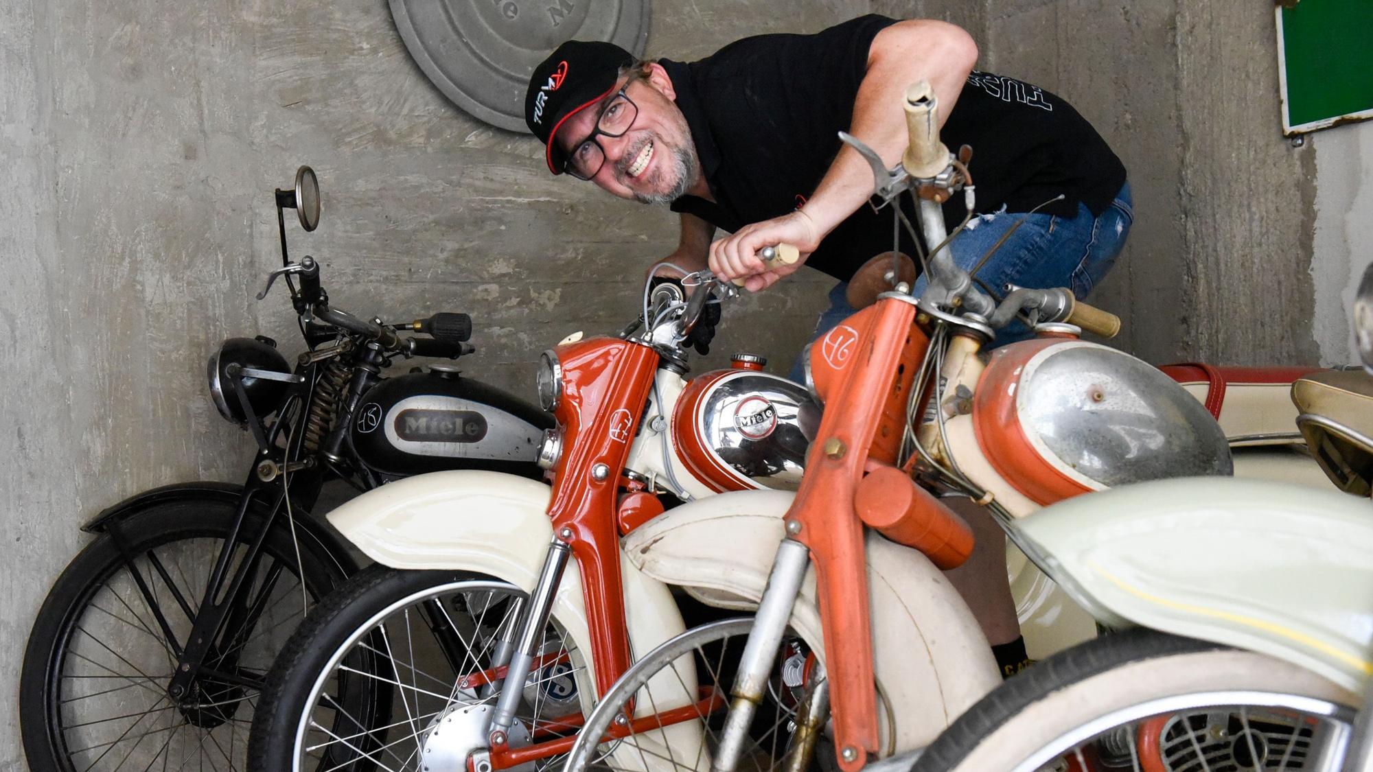 Das Foto zeigt vier historische Mopeds und einen Mann am Lenker.