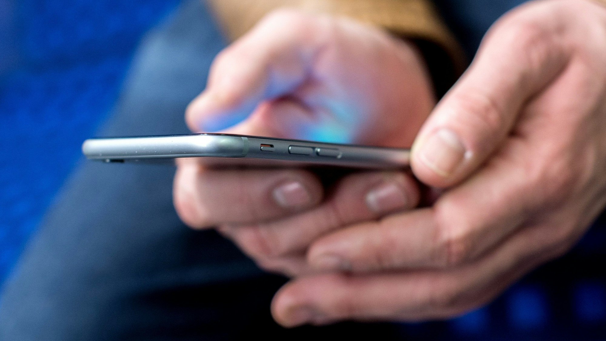Ein junger Mann sitzt in einer S-Bahn und benutzt dabei sein Smartphone.