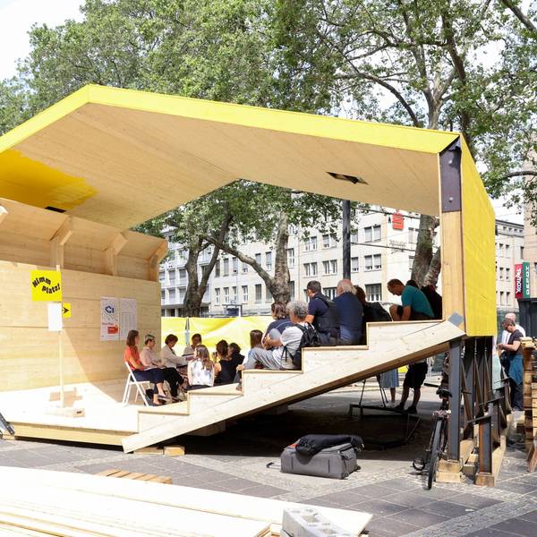 Ein Holzpavillon in gelber Farbe auf einem Platz.