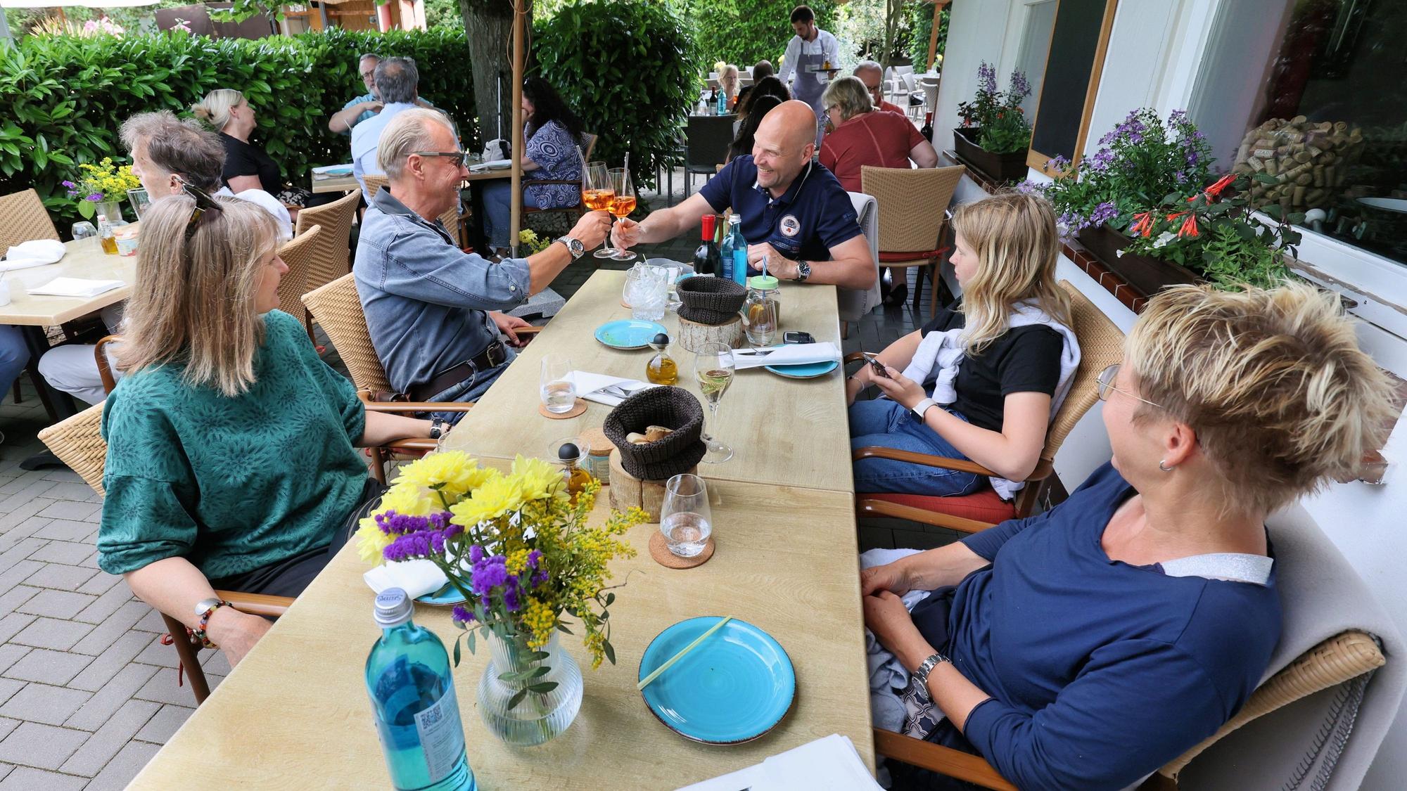 Leute sitzen an einem Biergartentisch und prosten sich zu.