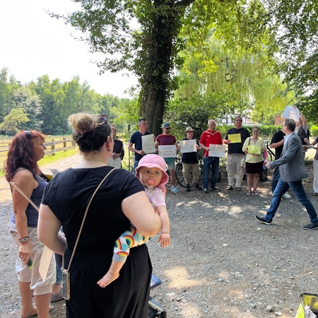 Mehrere Leute mit Schildern stehen auf einer Lichtung.