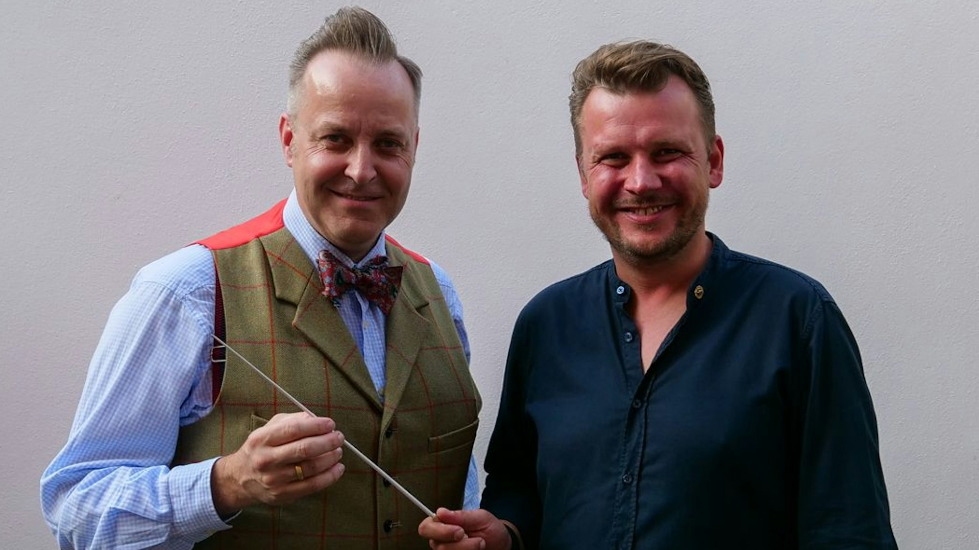 Das Foto zeigt zwei Männer bei der Übergabe eines Taktstocks.