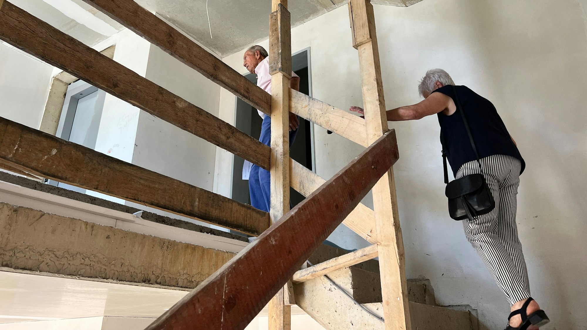 Zwei ältere Menschen gehen eine Holztreppe hoch.