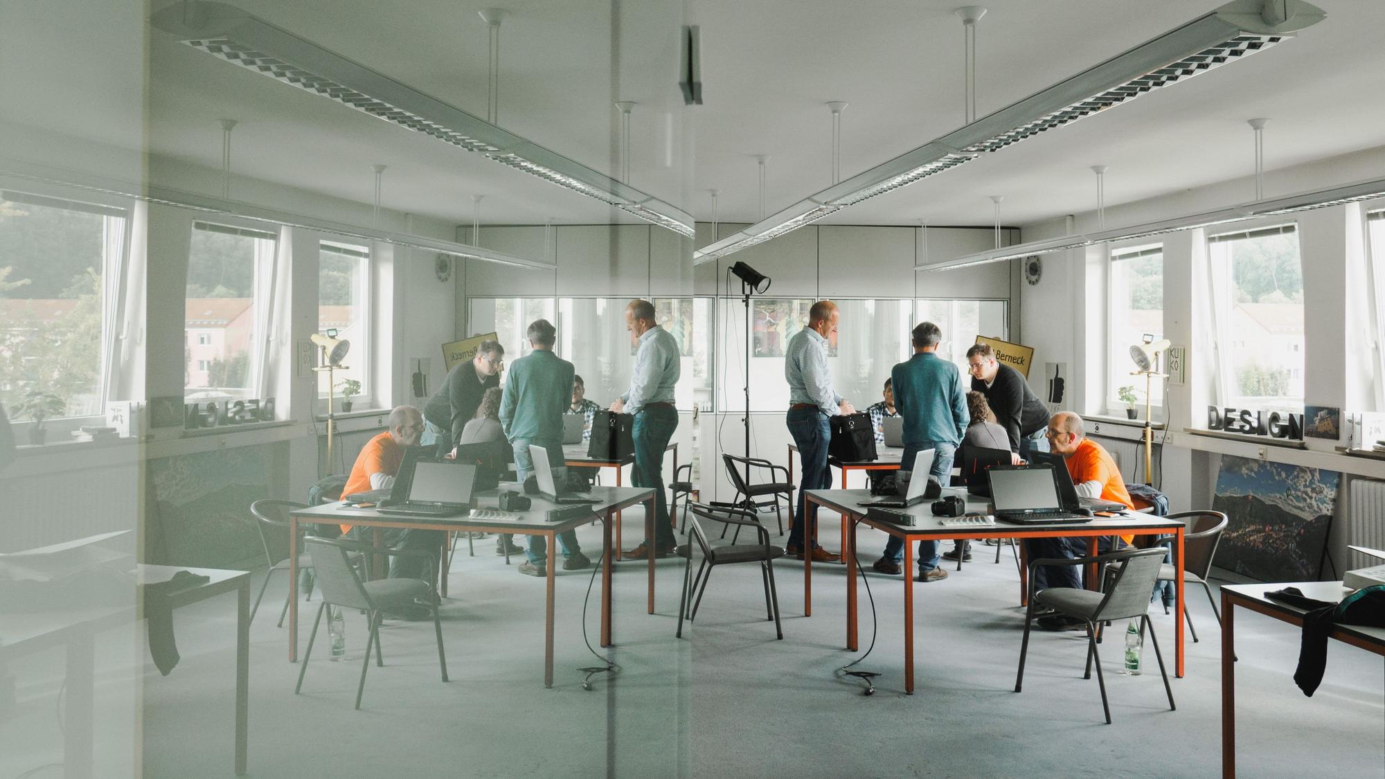 Wirtschaftsnacht Rheinland: Menschen arbeiten in einem minimalistischen Büro mit mehreren Arbeitsplätzen an zwei großen Tischen.
