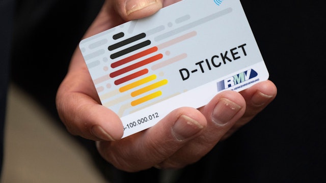 Zu sehen ist eine Hand, die ein Deutschlandticket in die Kamera hält.