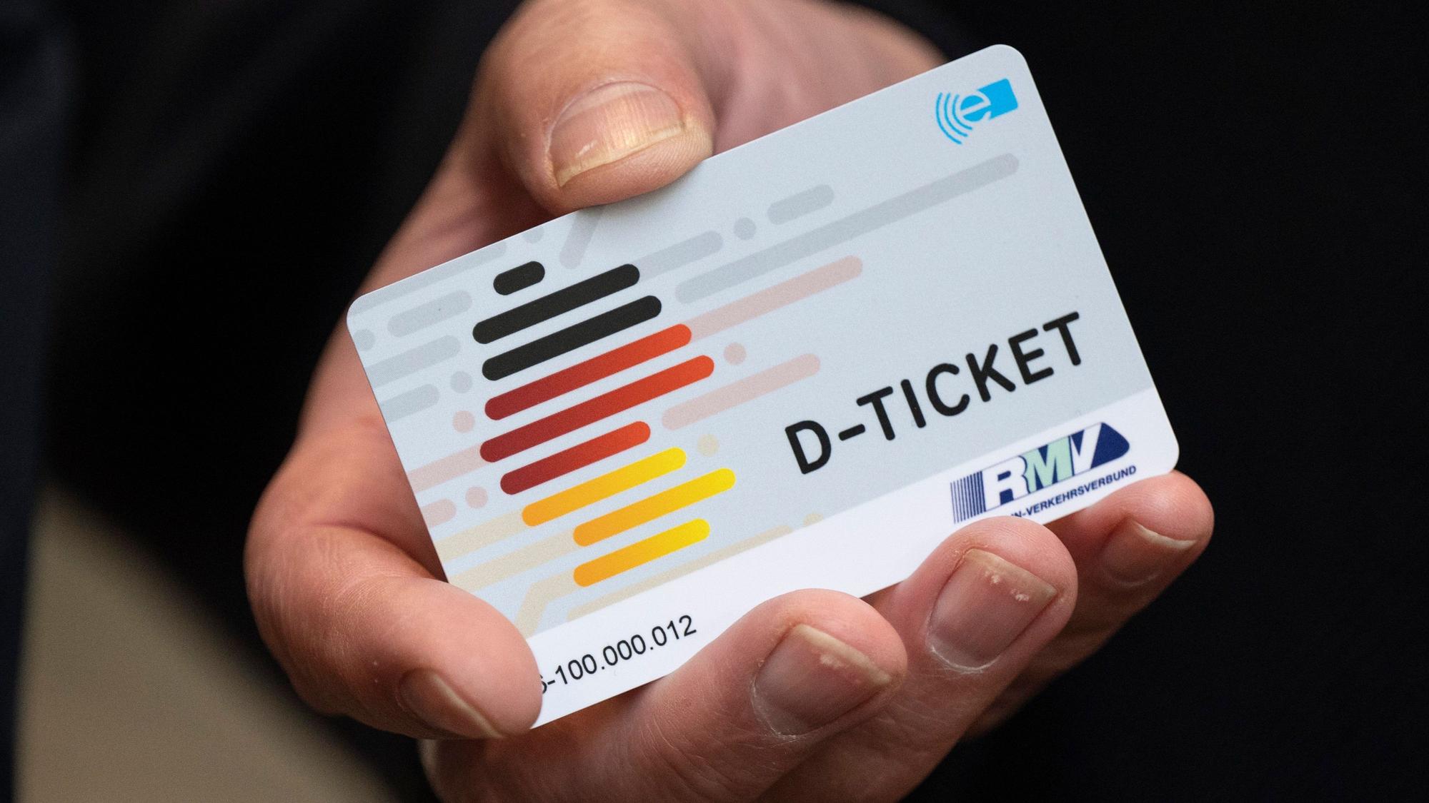 Zu sehen ist eine Hand, die ein Deutschlandticket in die Kamera hält.