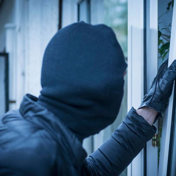 Ein maskierter Einbrecher versucht, ein Fenster zu öffnen.