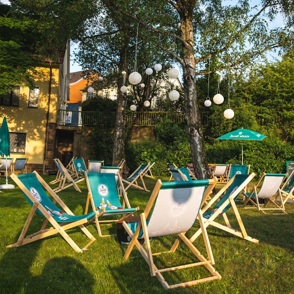 Auf einer Wiese stehen mehrere grüne Liegestühle mit Zunft Kölsch Logo.