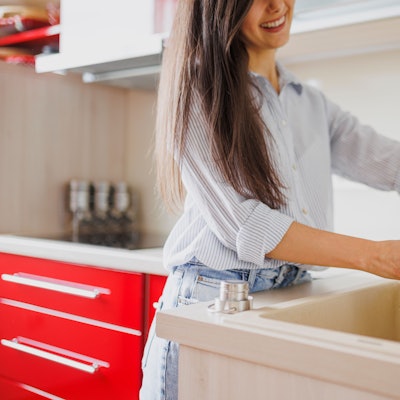 Eine Nahaufnahme einer Frau, die in der Küche eine wiederverwendbare Wasserflasche auffüllt.