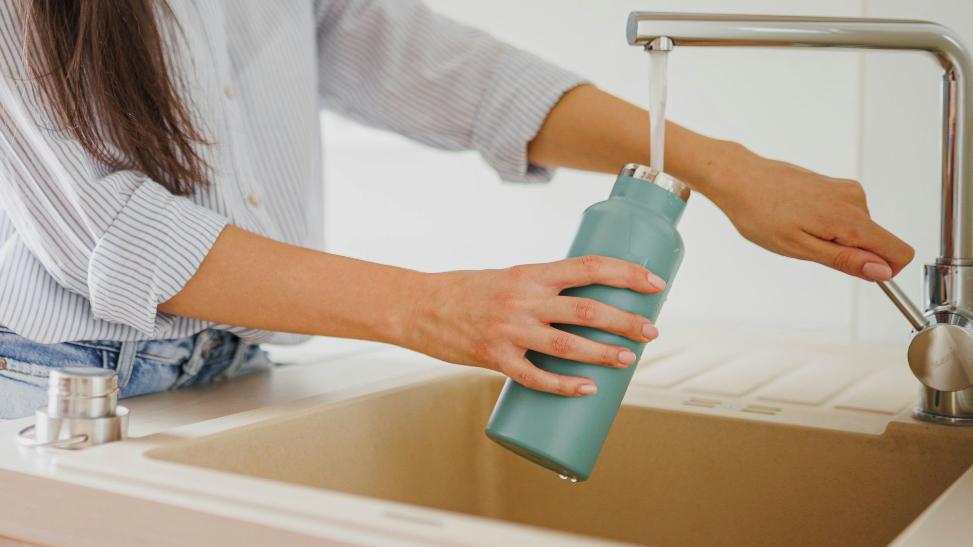 Eine Nahaufnahme einer Frau, die in der Küche eine wiederverwendbare Wasserflasche auffüllt.