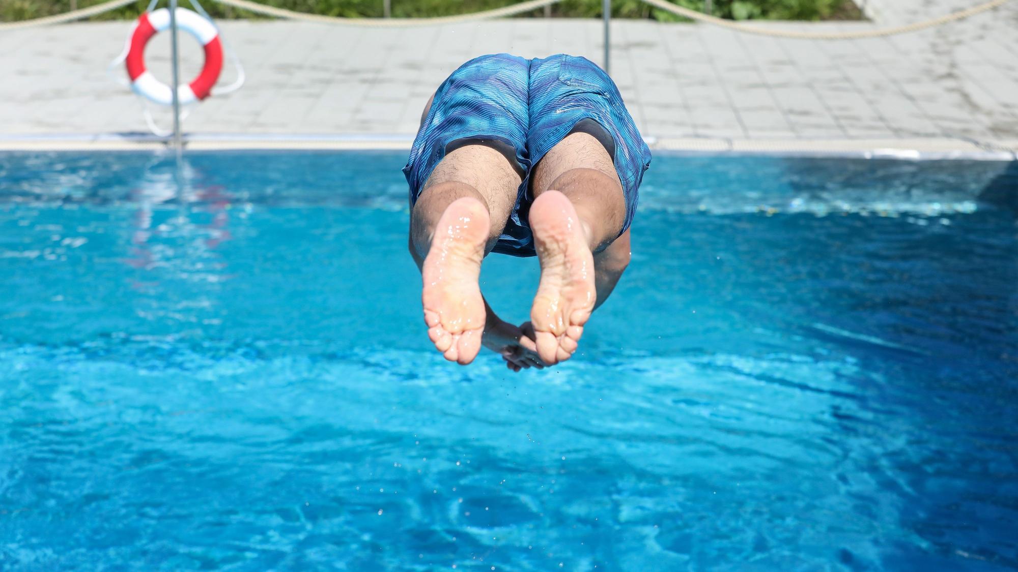 Ein Mann springt von einem Sprungbrett kopfüber ins Wasser.