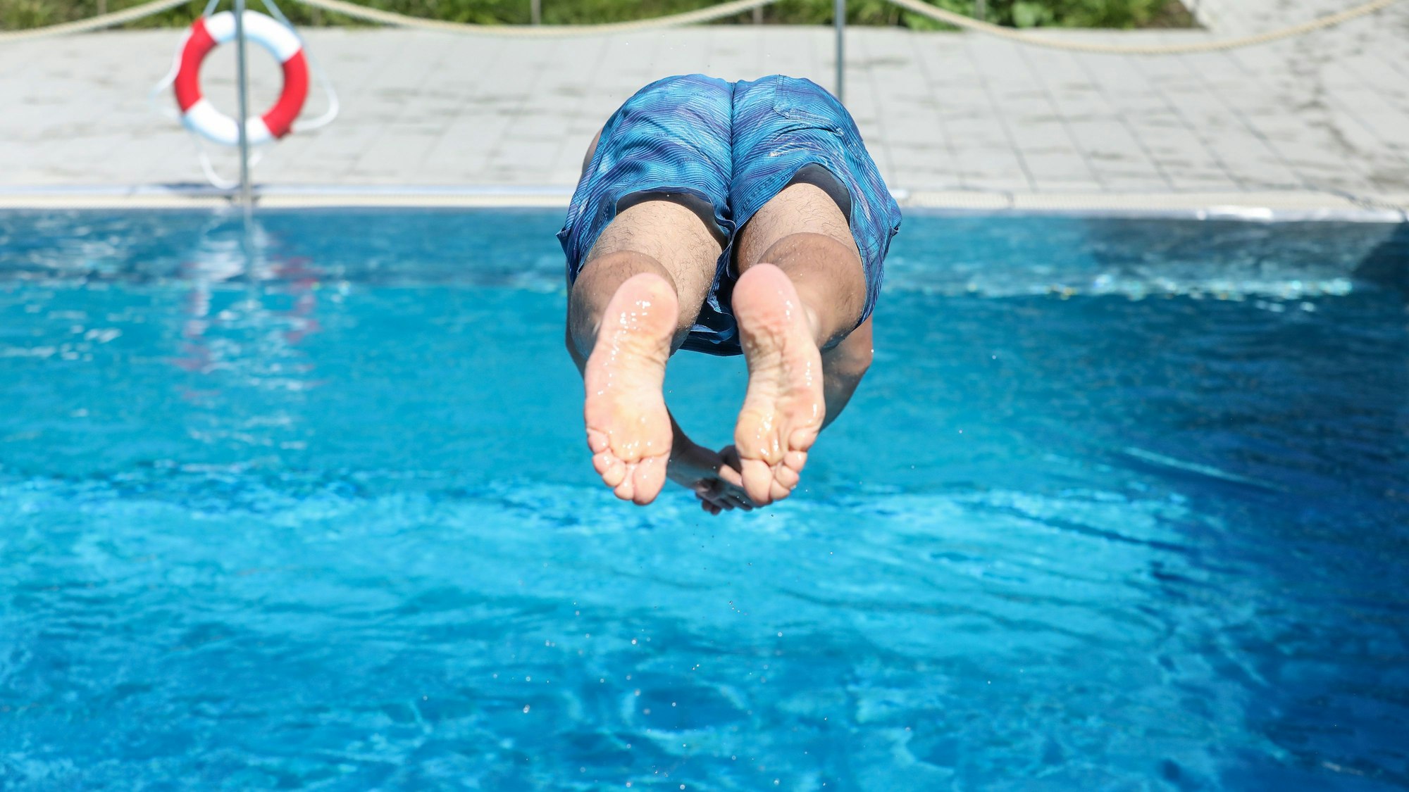 Ein Mann springt von einem Sprungbrett kopfüber ins Wasser.