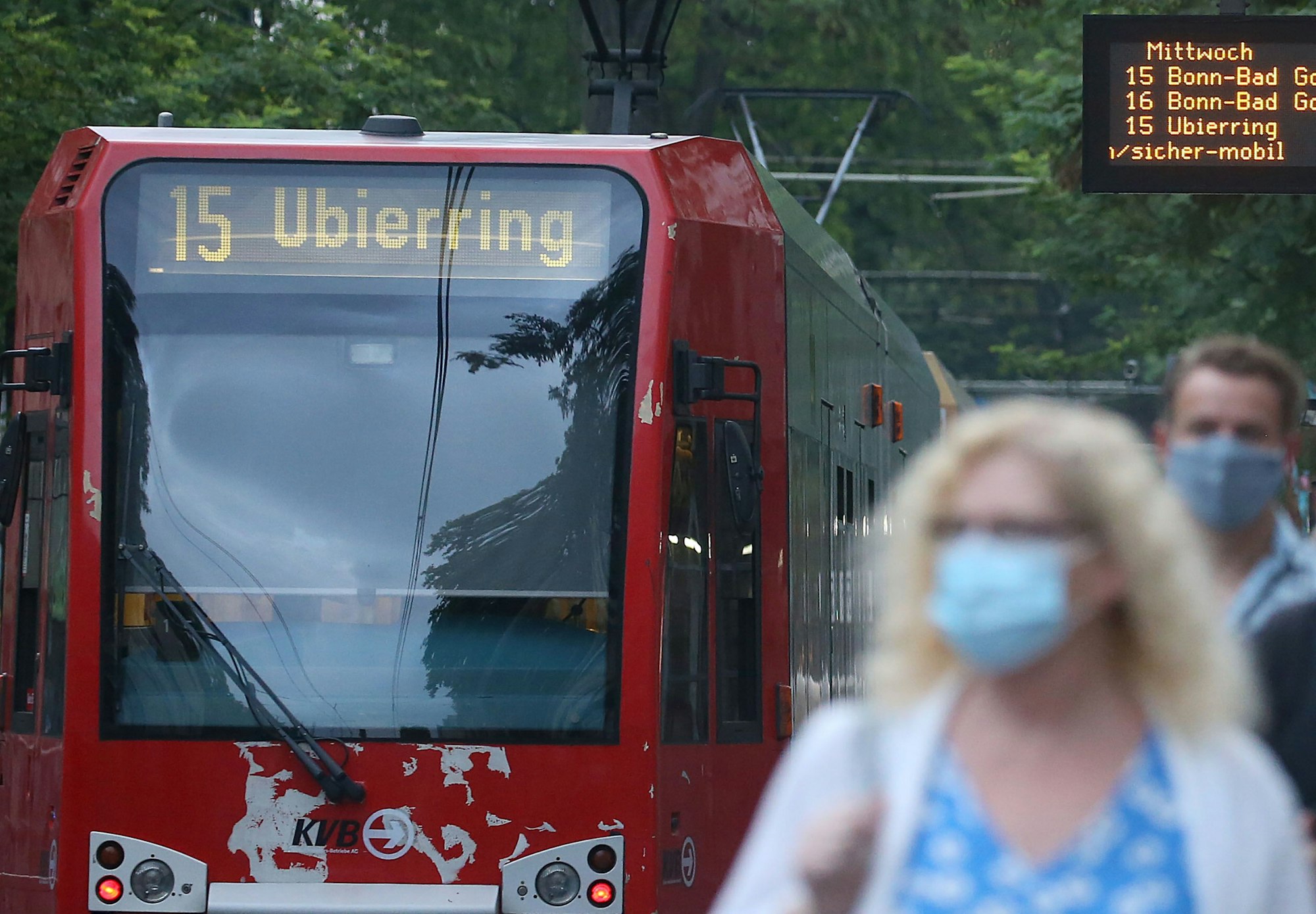 Fahrgäste verlassen einen Bahnsteig neben einer Straßenbahn. Sie tragen Masken.