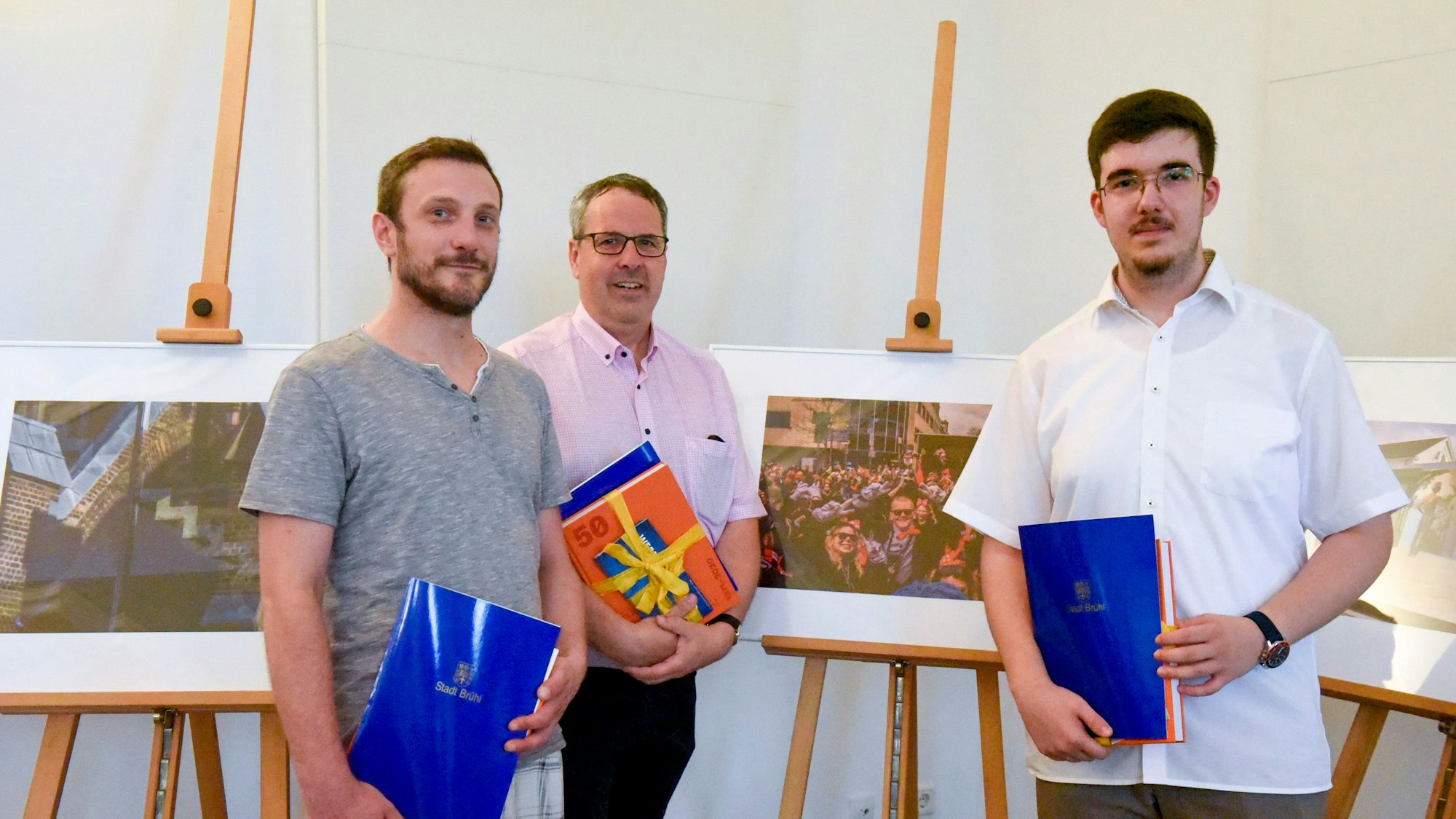 Die drei Gewinner des Fotopreises stehen vor ihren Bildern und halten Urkunden in der Hand.