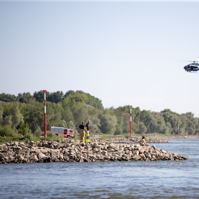 Aus einem Hubschrauber und vom Ufer aus suchen Einsatzkräfte nach einem Schwimmer, der im Rheim von einem Sog erfasst und mitgerissen wurde.