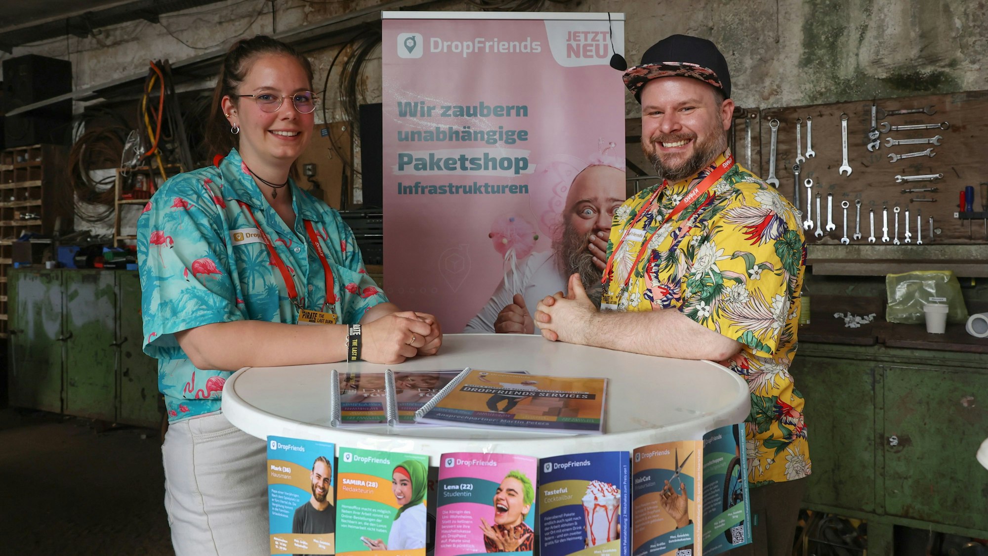 Drop-Friends-Gründer Martin Peters und Mitarbeiterin Johanna Haerther bei der weltweit beachteten Start-up-Konferenz Pirate Summit im Odonien. Sie tragen Hawaii-Hemden und lehnen an einem Stehtisch mit Flyern.