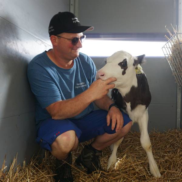 Landwirt Sebastian Bützler kniet neben einem Kalb.