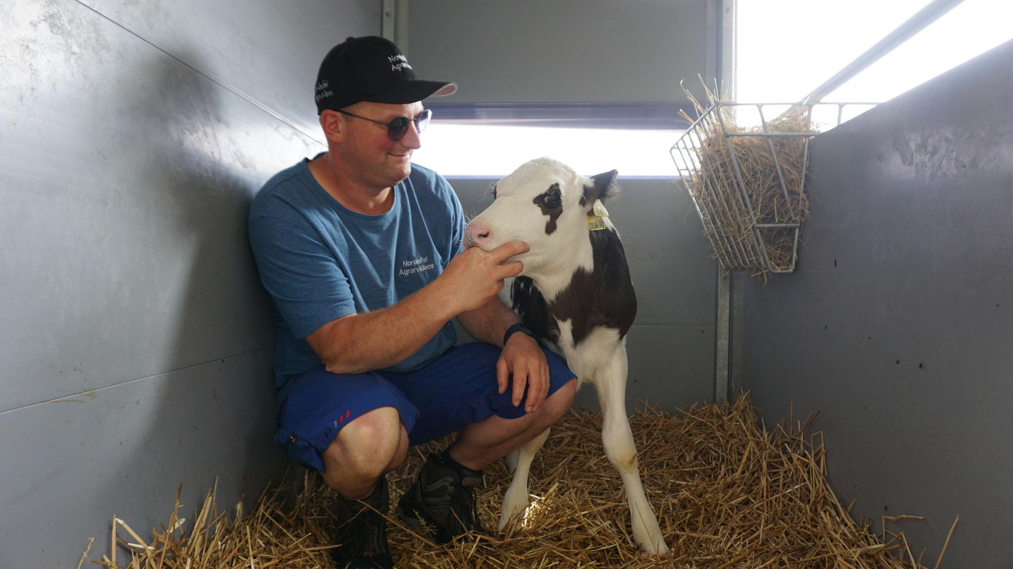 Landwirt Sebastian Bützler kniet neben einem Kalb.