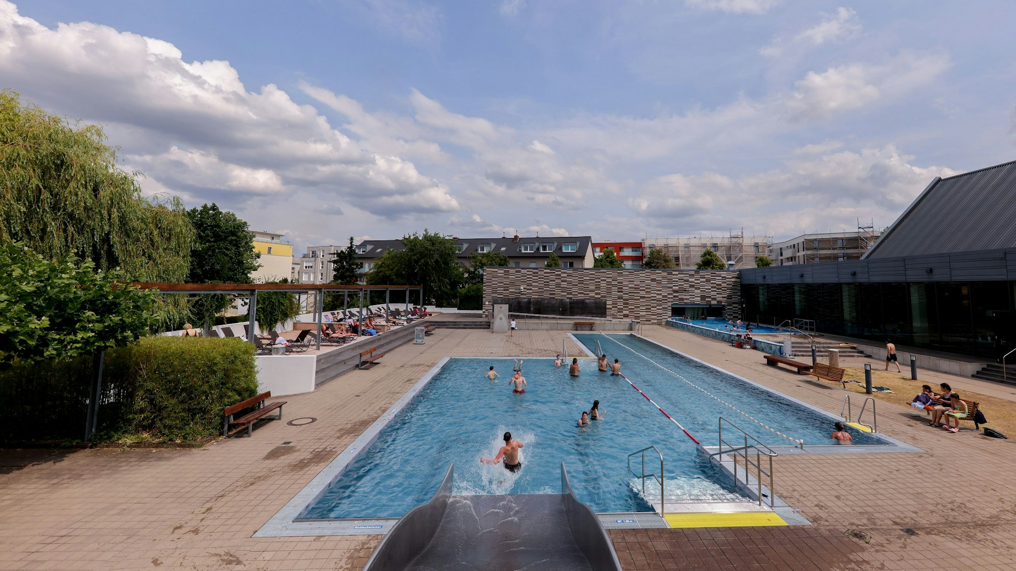 Das Freibad von weiter weg fotografiert, mit Schwimmbecken und Liege-Terrasse.