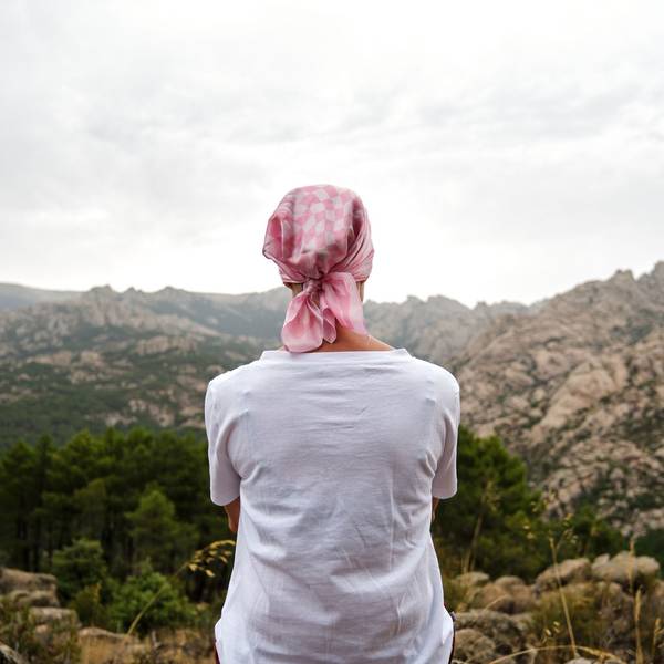 Eine Frau mit Kopftuch sitzt auf einem Berg und schaut in die Landschaft.