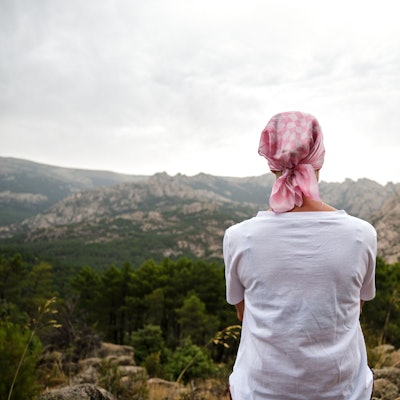 Eine Frau mit Kopftuch sitzt auf einem Berg und schaut in die Landschaft.