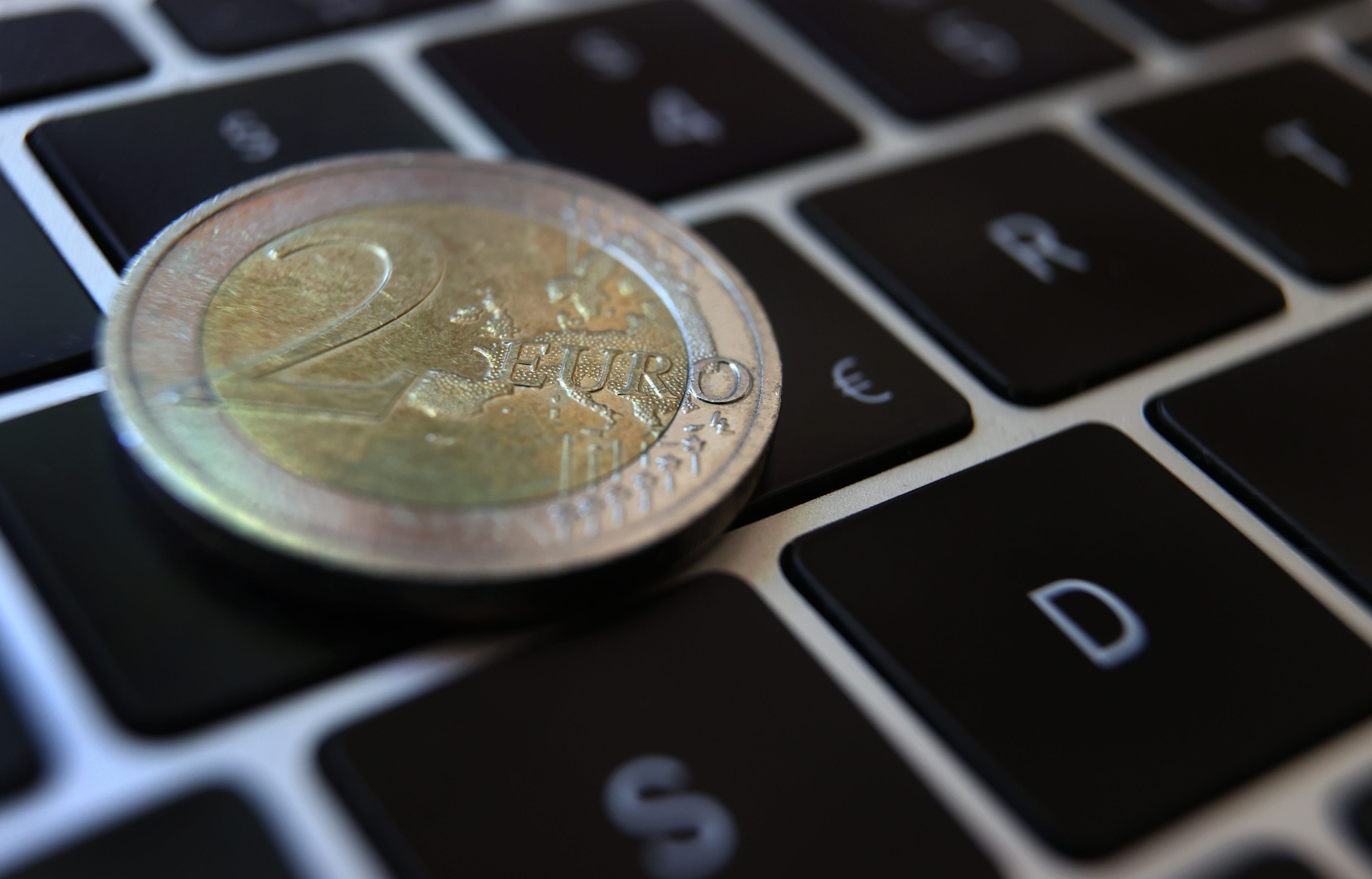 Eine Zwei-Euro-Münze liegt auf der Tastatur eines Laptops neben einem Eurozeichen.