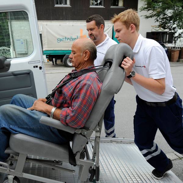 Ein Freiwilligendienstler übt, wie man einen Gehbinderten Menschen in einen Transporter schiebt.