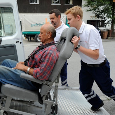 Ein Freiwilligendienstler übt, wie man einen Gehbinderten Menschen in einen Transporter schiebt.