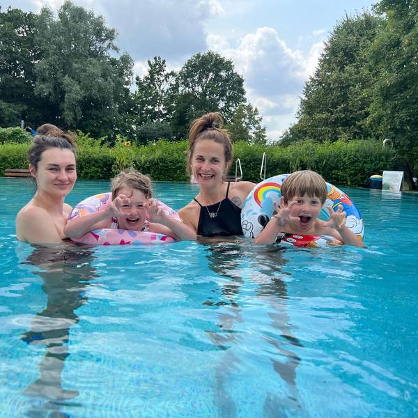 Zwei junge Mütter und ihre zwei Kinder posieren im Wasser für ein Foto.