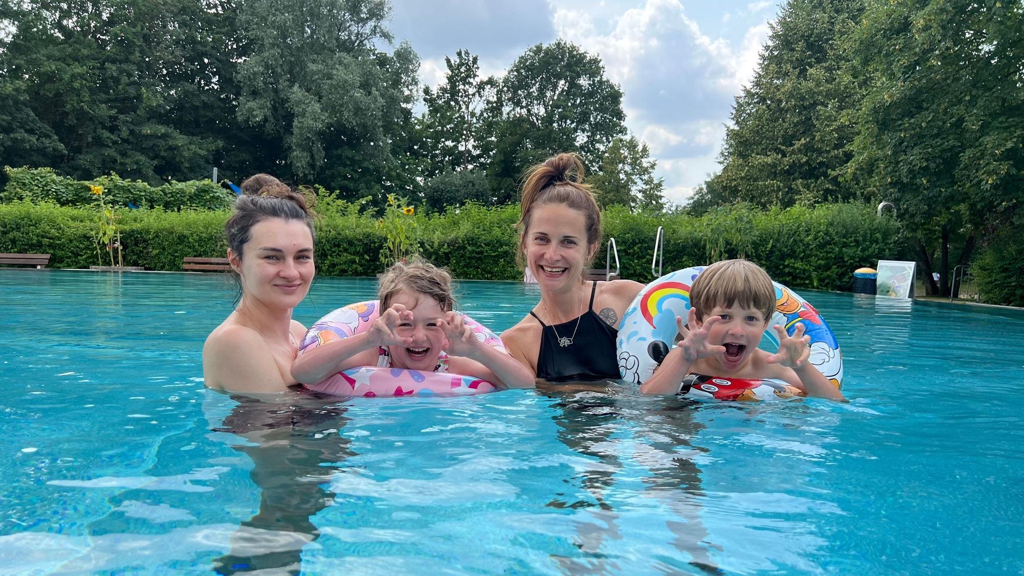 Zwei junge Mütter und ihre zwei Kinder posieren im Wasser für ein Foto.
