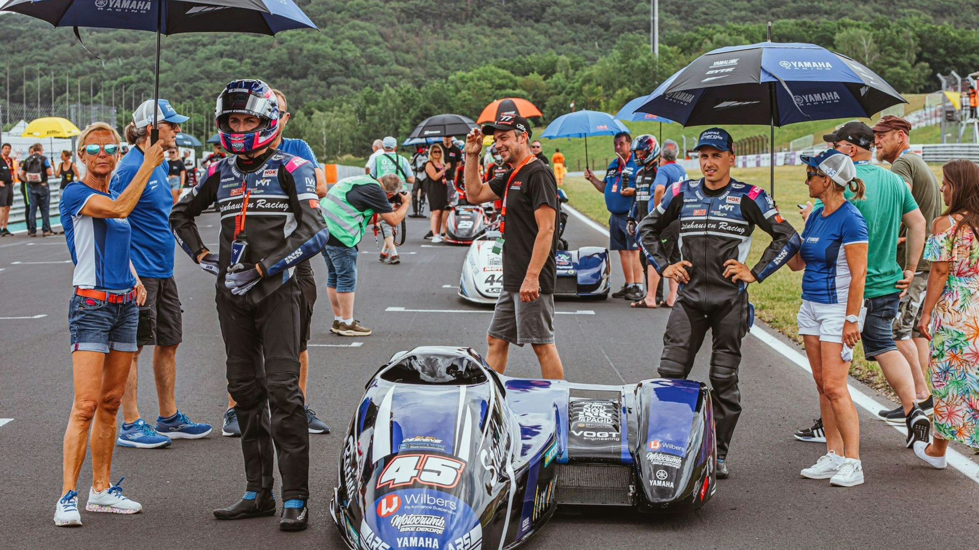 Zu sehen sind Frauen, die Schirme über Rennfahrer halten.