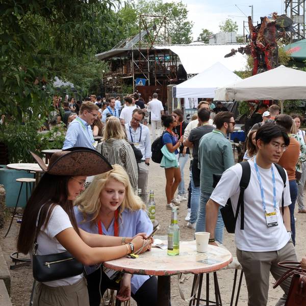 Die weltweit beachtete Start-up-Konferenz Pirate Summit findet zum letzten Mal in Odonien statt: Menschen an Stehtischen unter Sonnenschirmen in der Ehrenfelder Kutlurstätte.