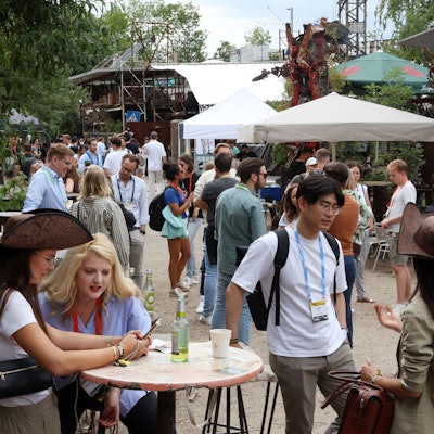 Die weltweit beachtete Start-up-Konferenz Pirate Summit findet zum letzten Mal in Odonien statt: Menschen an Stehtischen unter Sonnenschirmen in der Ehrenfelder Kutlurstätte.