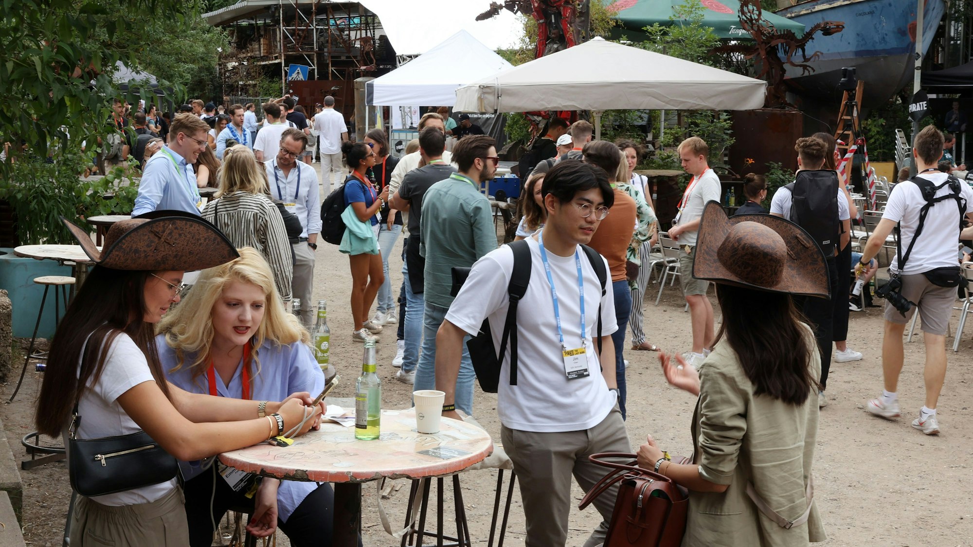 Die weltweit beachtete Start-up-Konferenz Pirate Summit findet zum letzten Mal in Odonien statt: Menschen an Stehtischen unter Sonnenschirmen in der Ehrenfelder Kutlurstätte.