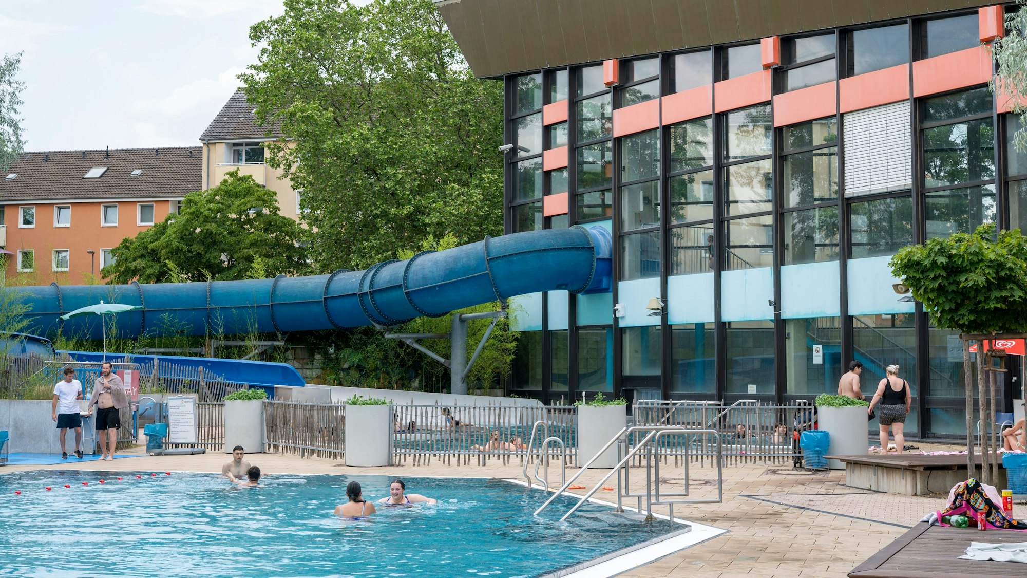 Außenbereich des Höhenbergbads mit einem Schwimmbecken im Vorder- und dem Gebäude sowie einer langen Rutsche im Hintergrund