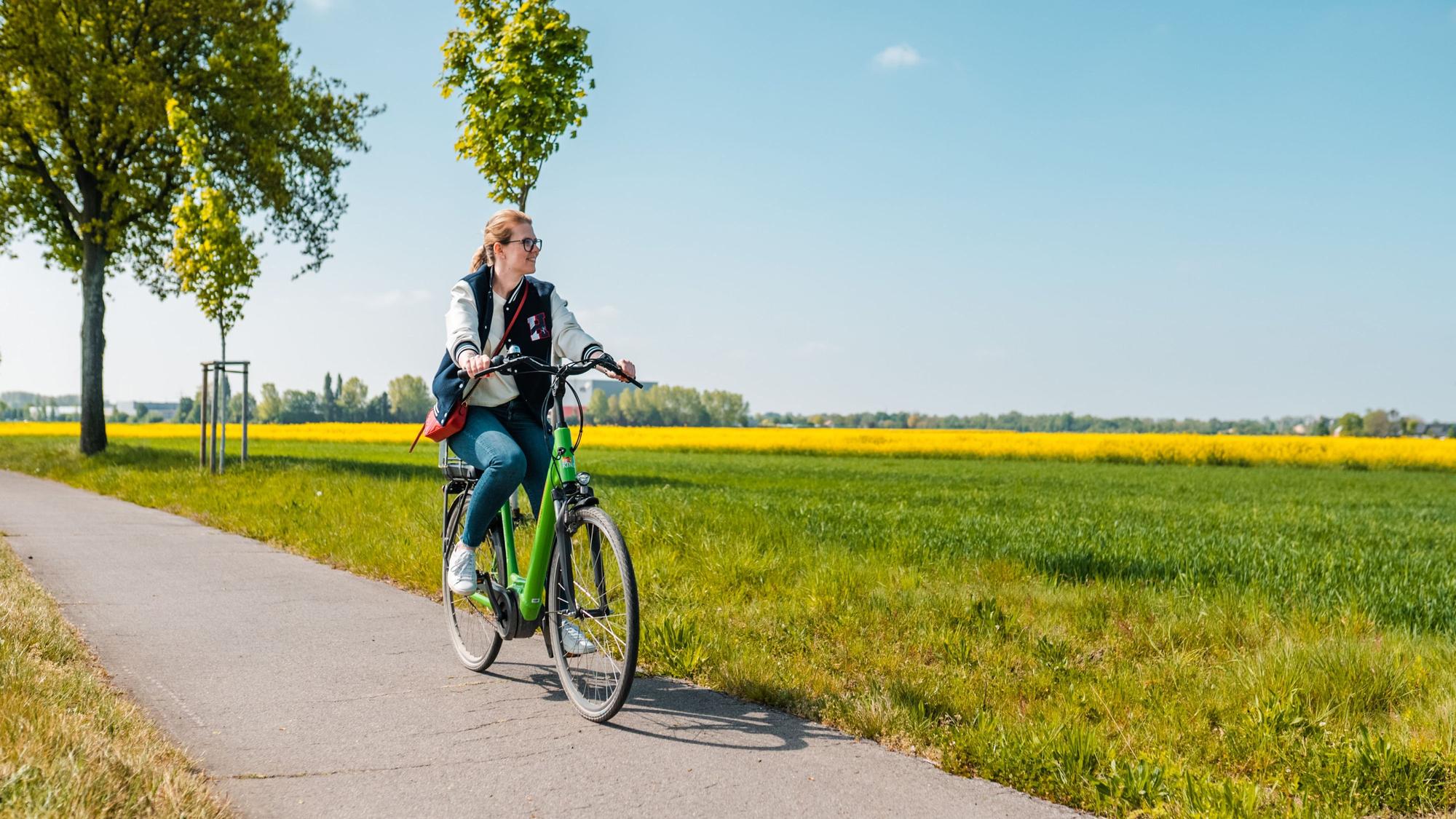 Frau fährt auf einem Fahrrad zwischen Wiesen hindurch