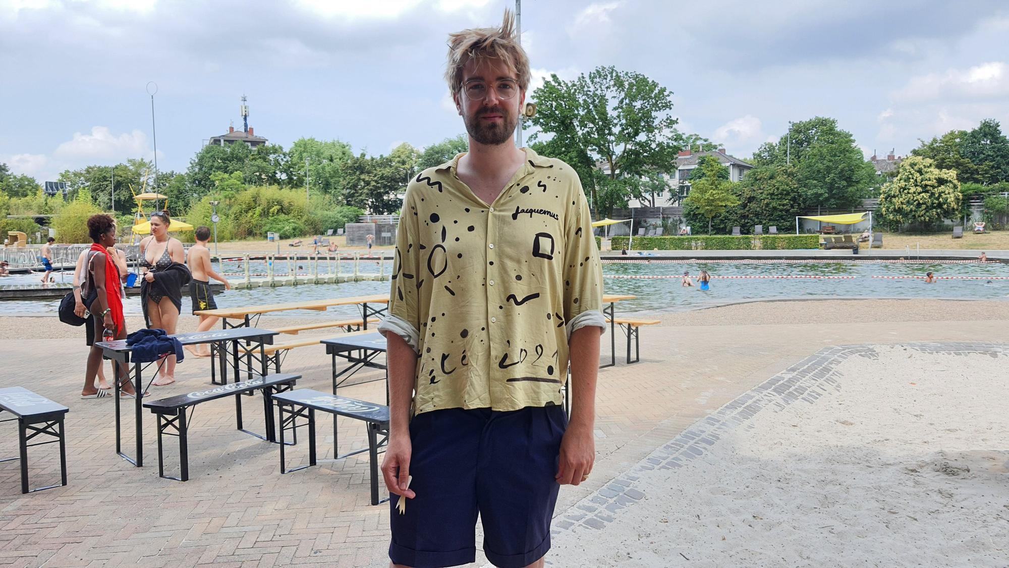 Ein Mann in Hemd und Hose steht vor einem Schwimmbecken.