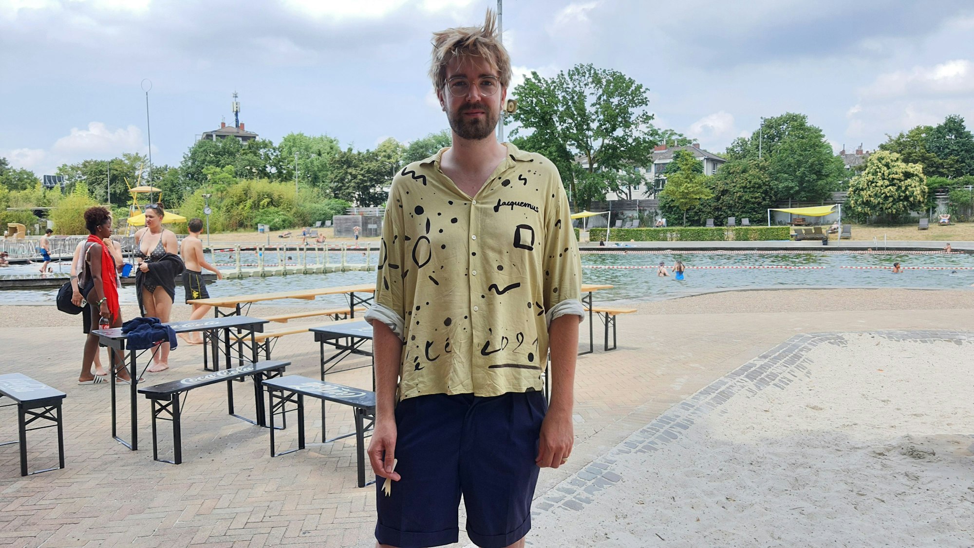 Ein Mann in Hemd und Hose steht vor einem Schwimmbecken.