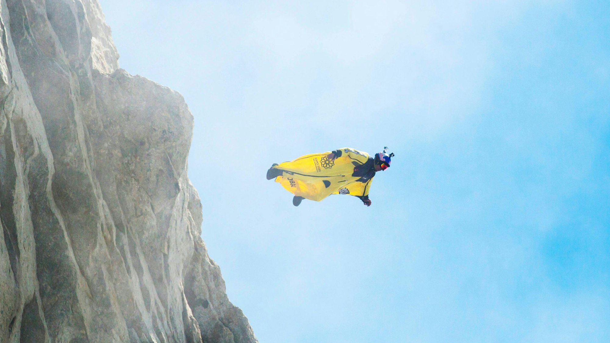 Ein Basejumper in einem gelben Wingsuit springt von einem Felsen (Symbolbild)