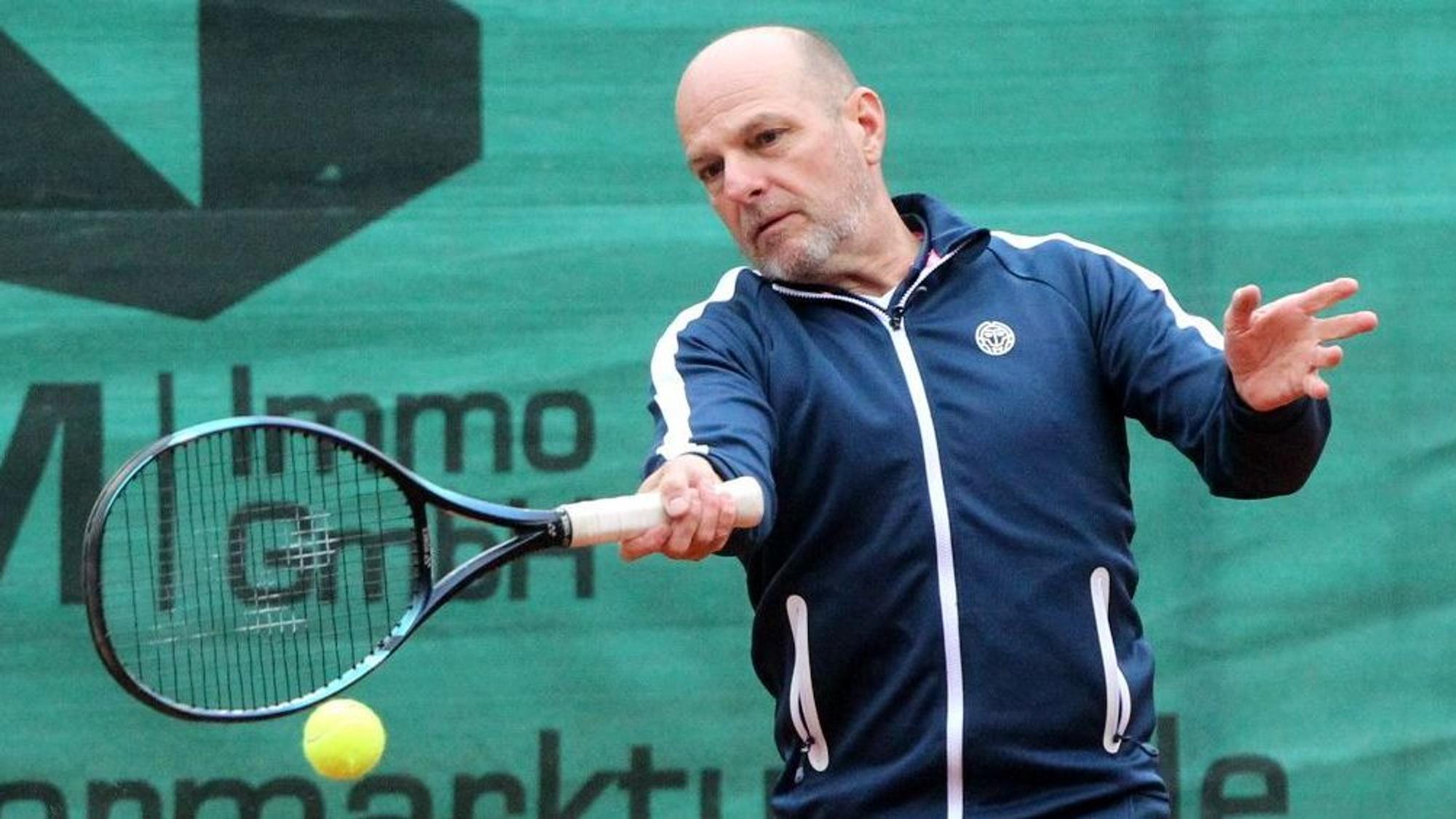 Ein Tennisspieler im Trainingsanzug schlägt einen Ball.