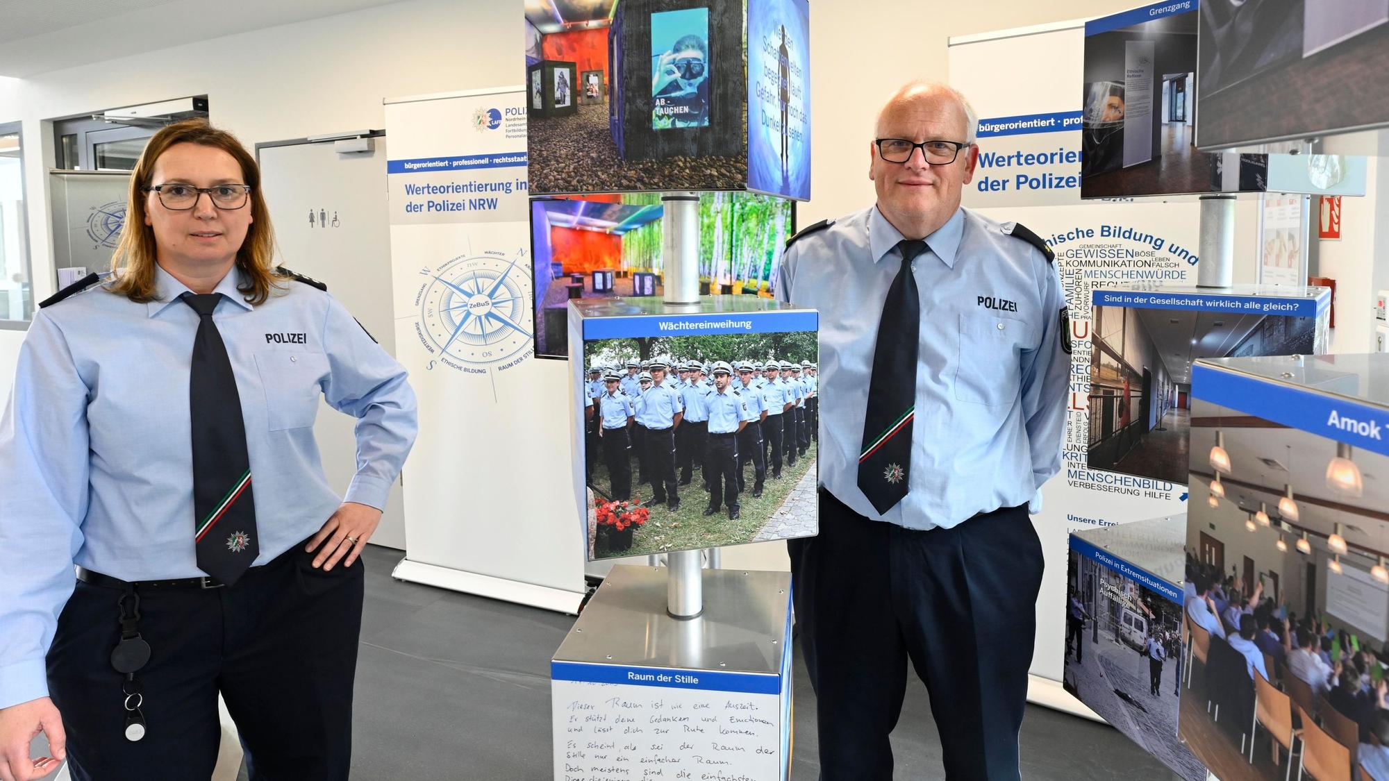 Eine Polizeibeamtin und ihr Kollegen stehen in Uniform zwischen den Tafeln einer Ausstellung.